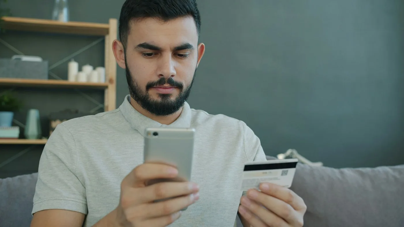 Pessoa conferindo um celular enquanto segura um cartão